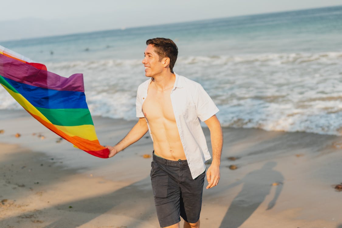 Бесплатные стоковые фото на тему выражение лица, гей, держать, лгбт,  мужчина, пляж, радужный флаг, улыбаться