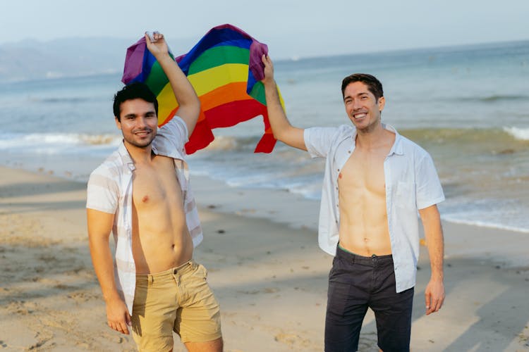 Gay Men Standing On A Beach And Holding A Rainbow Flag 