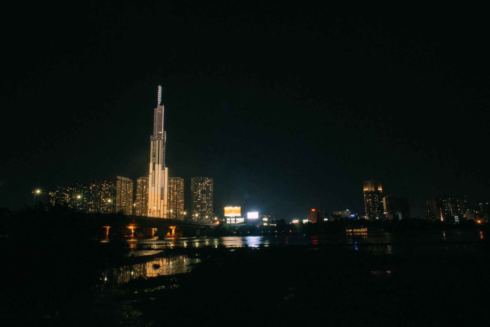 Landmark 81 and the Saigon skyline lit at night, reflected in the river