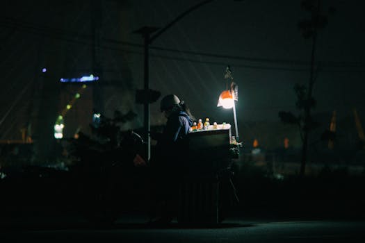 A street vendor sells bottled drinks from an illuminated cart on a Vietnam street at night.
