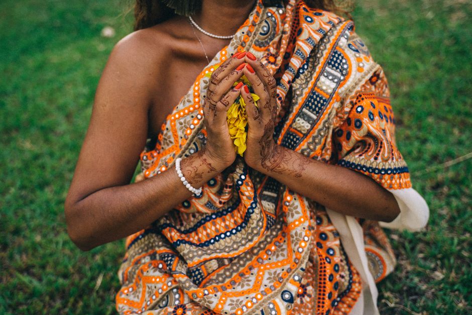 A close-up of clasped hands with mehndi and flowers in an Indian saree, depicting cultural elegance.