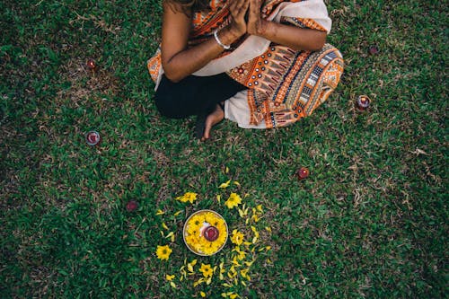 Woman in a Traditional Saree Dress Sitting on the Grass with a Plate with Flowers and a Candle