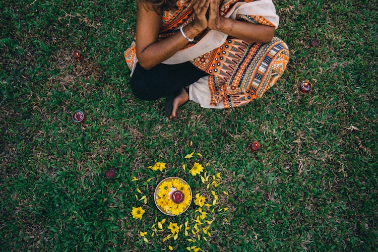 Woman In A Traditional Saree Dress Sitting On The Grass With A Plate With Flowers And A Candle