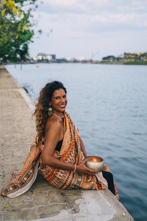 Woman in a Traditional Saree Dress Sitting by the Water and Smiling 