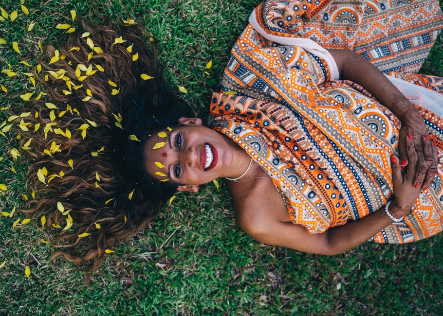 Smiling woman in a colorful sari lying on grass with yellow petals, showcasing cultural beauty.
