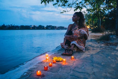 A Woman Sitting Near the Lighted Candles while Looking at the Sea