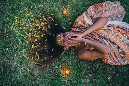 Indian woman lying on grass, adorned with henna and vibrant sari, surrounded by candlelight, creating a serene atmosphere.