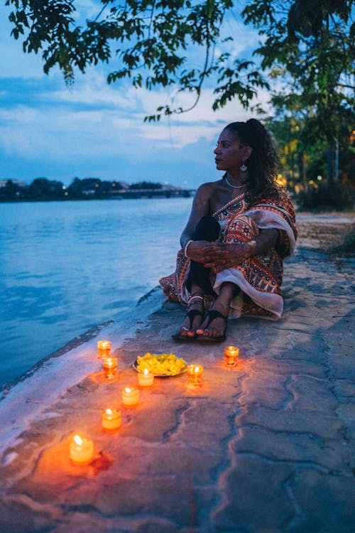 Woman in a Traditional Saree Dress Sitting by the Water with Candles 