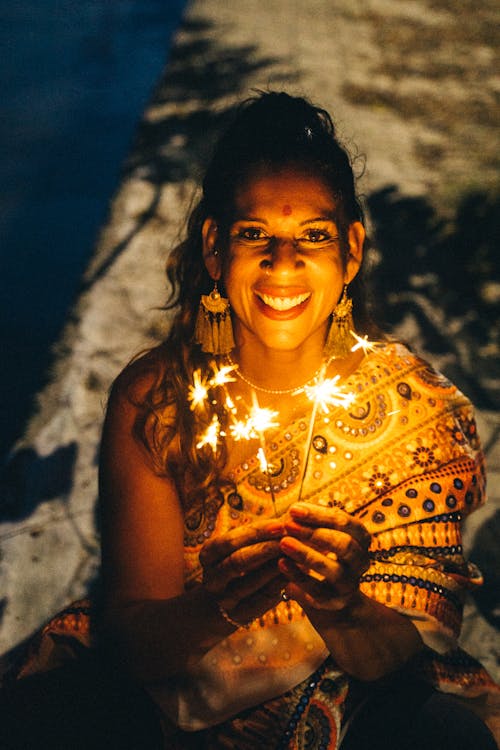 Smiling Woman in Yellow Saree Holding Lighted Sparklers