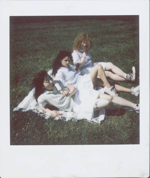 Polaroid Picture of Women Eating Popsicles while Sitting on a Picnic Blanket