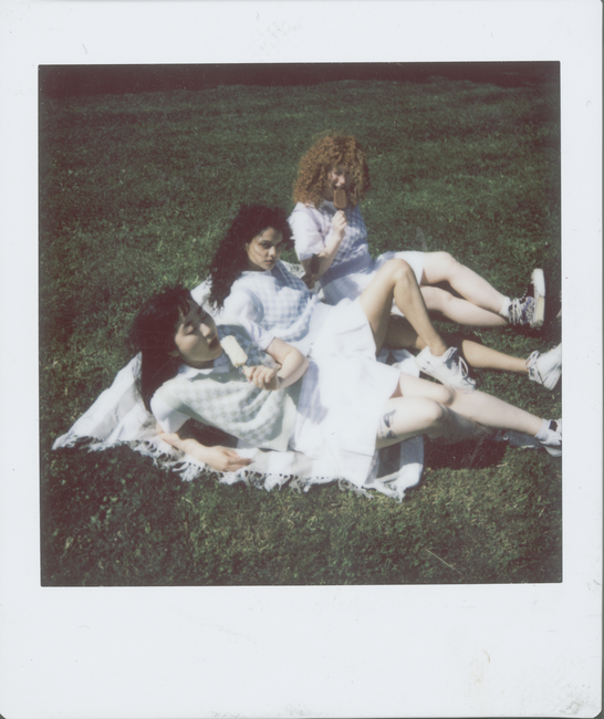 Three women enjoying a sunny picnic, lying on a blanket in a grassy field.