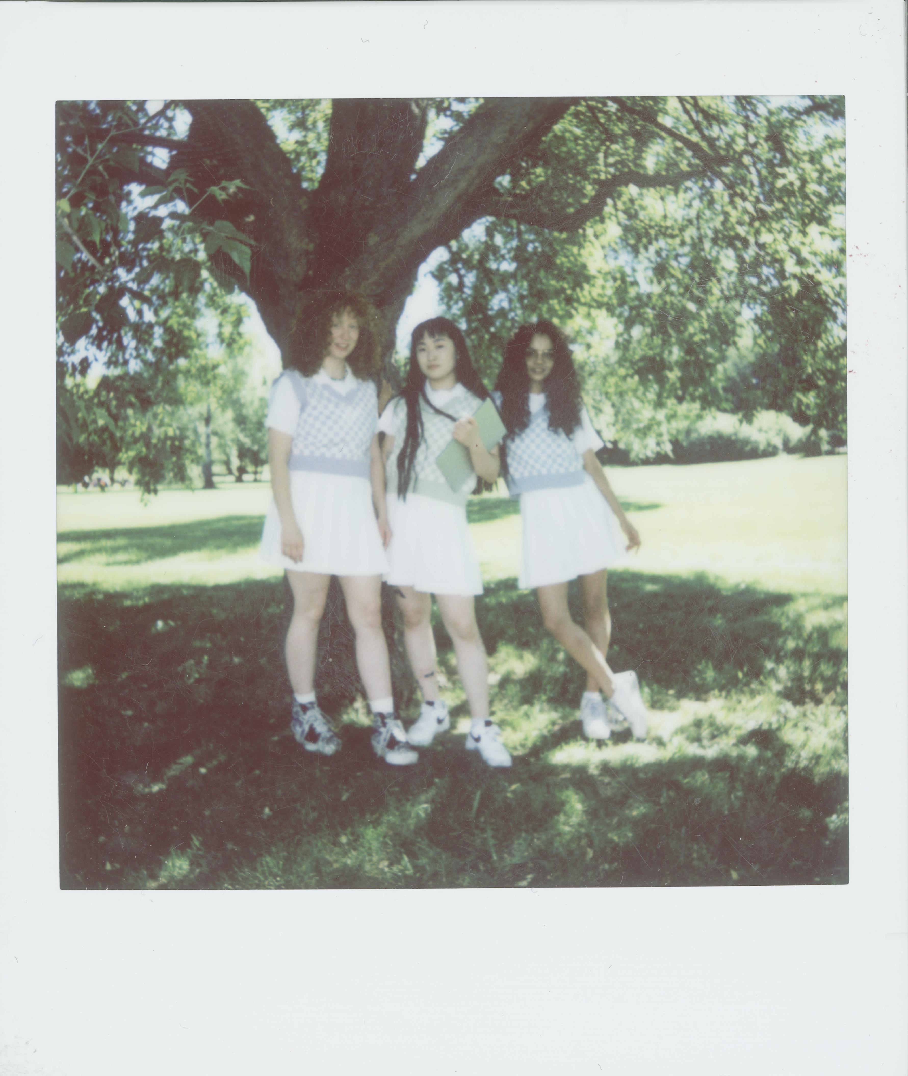Three teenage girls in school uniforms posing under a tree during a sunny day, evoking a back-to-school theme.