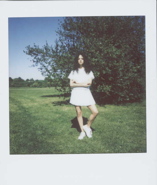 A young woman stands confidently in a sunlit field, embodying youth and style.