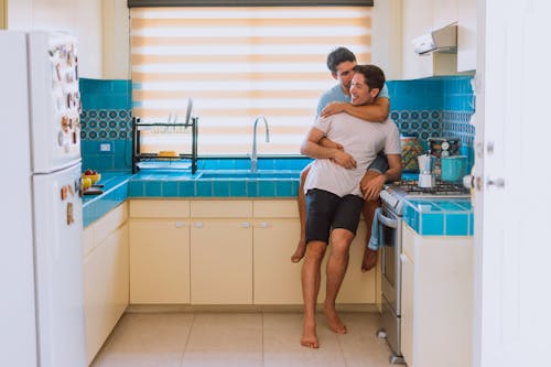 Free Man Sitting on Kitchen Counter While Hugging Another Man Stock Photo