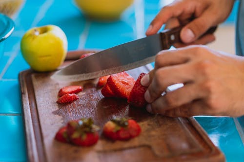 Person Slicing Strawberries on Wooden Chopping Board