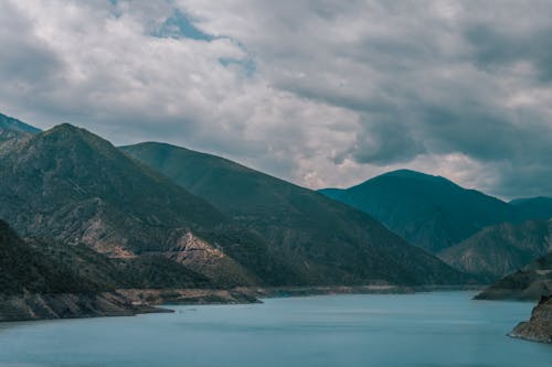 Body of Water and Mountains Under Cloudy Sky