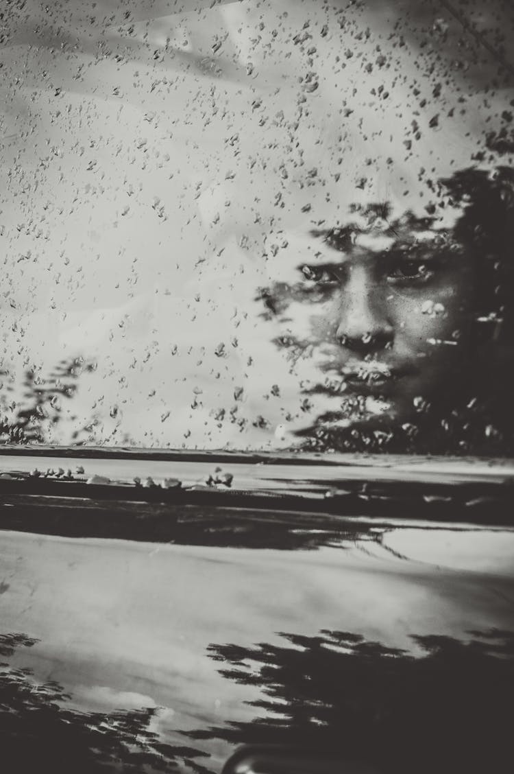 Man Behind A Car Window Covered In Raindrops And Reflecting Light 