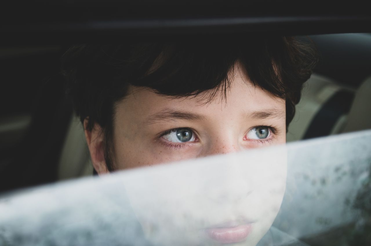 close up of a young child looking through a misted car window lost in