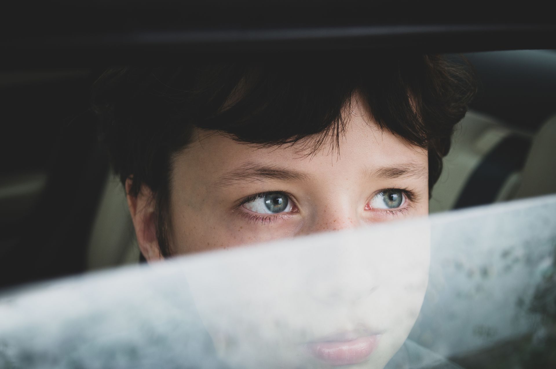 Close-up of a young child looking through a misted car window, lost in thought.