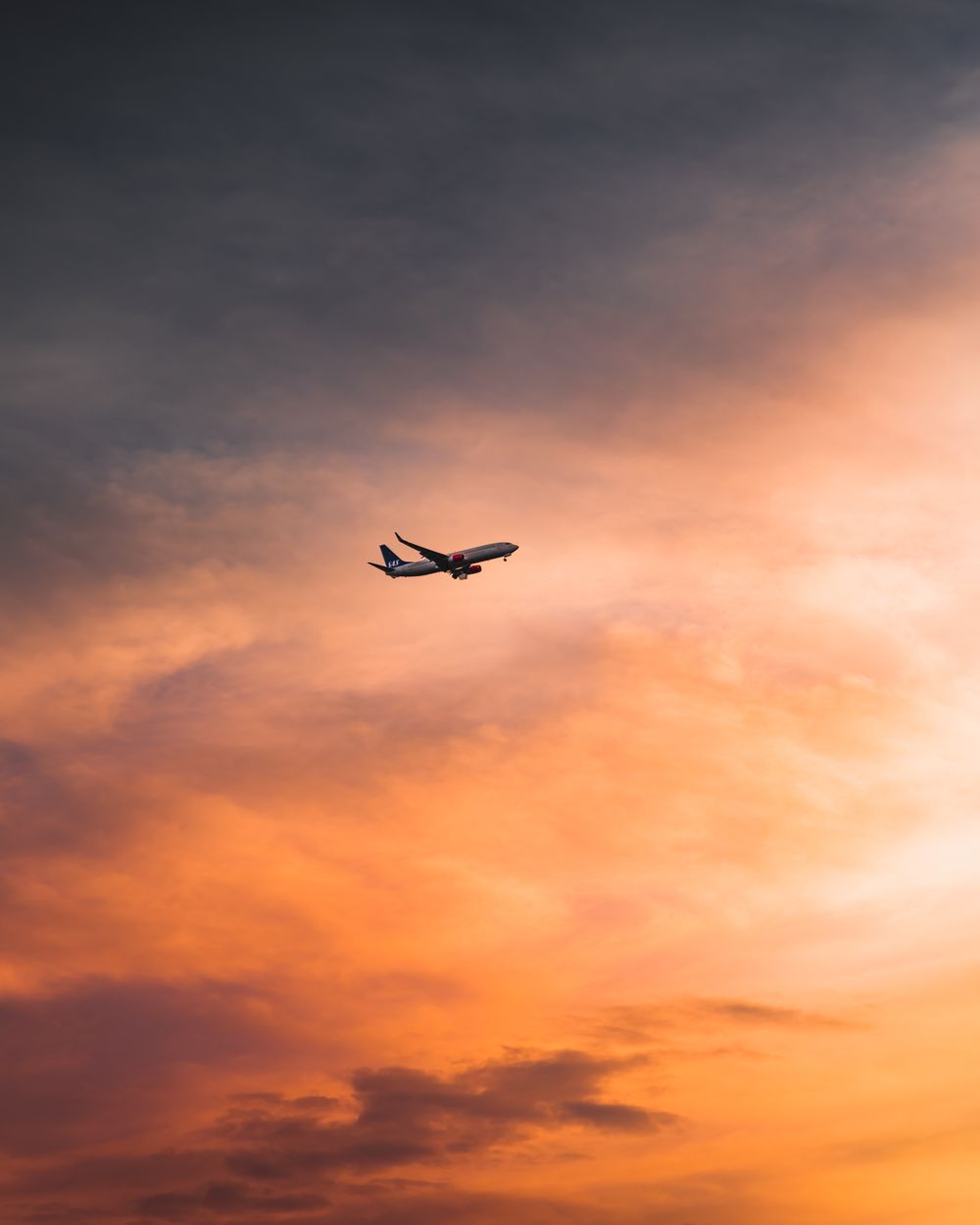 Commercial aircraft crossing a vivid orange sunset sky, creating a striking silhouette