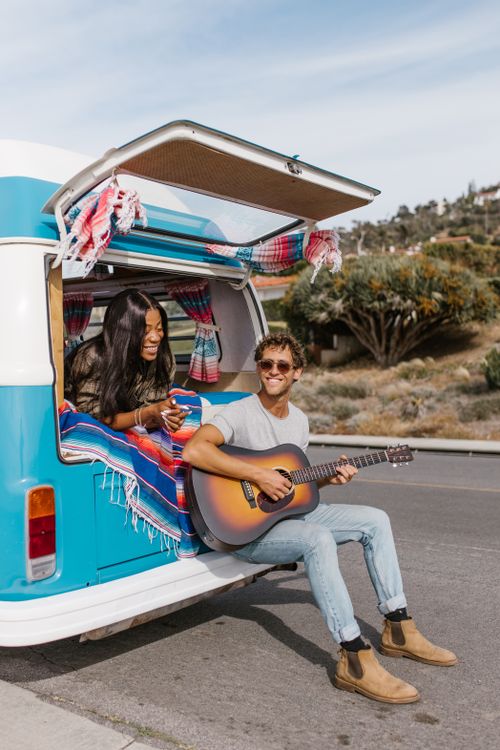 Free A joyful couple relaxes with guitar music near their retro camper van. Stock Photo