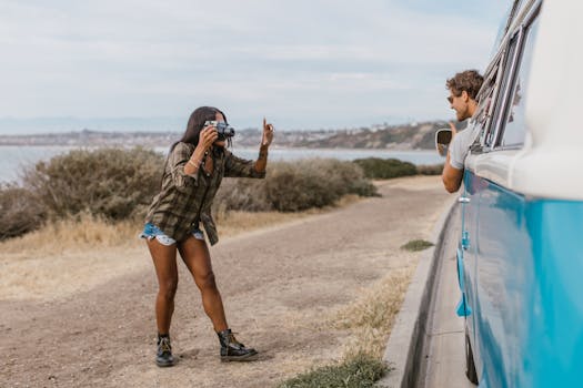 Woman takes picture of man in a van by the coast, showcasing travel and lifestyle.