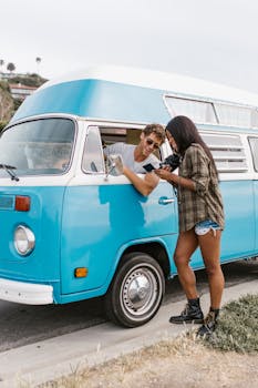 A man and woman enjoying a road trip in a classic blue campervan, exuding adventure and fun.