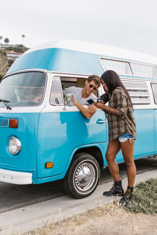 Free A man and woman enjoying a road trip in a classic blue campervan, exuding adventure and fun. Stock Photo