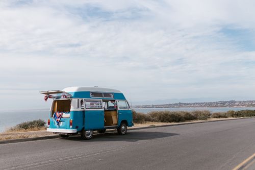 Free A classic blue van parked along a scenic coastal road under a cloudy sky. Stock Photo