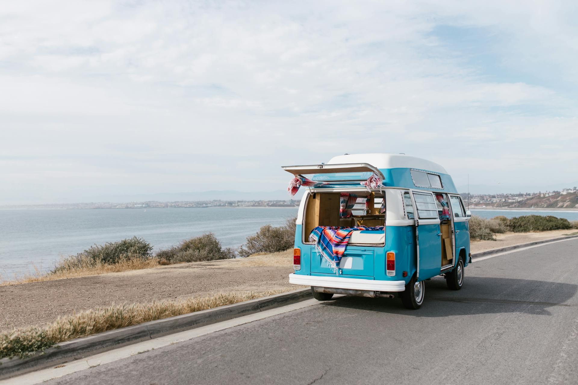 A classic blue camper van parked by the sea on a sunny day, perfect for a coastal road adventure.