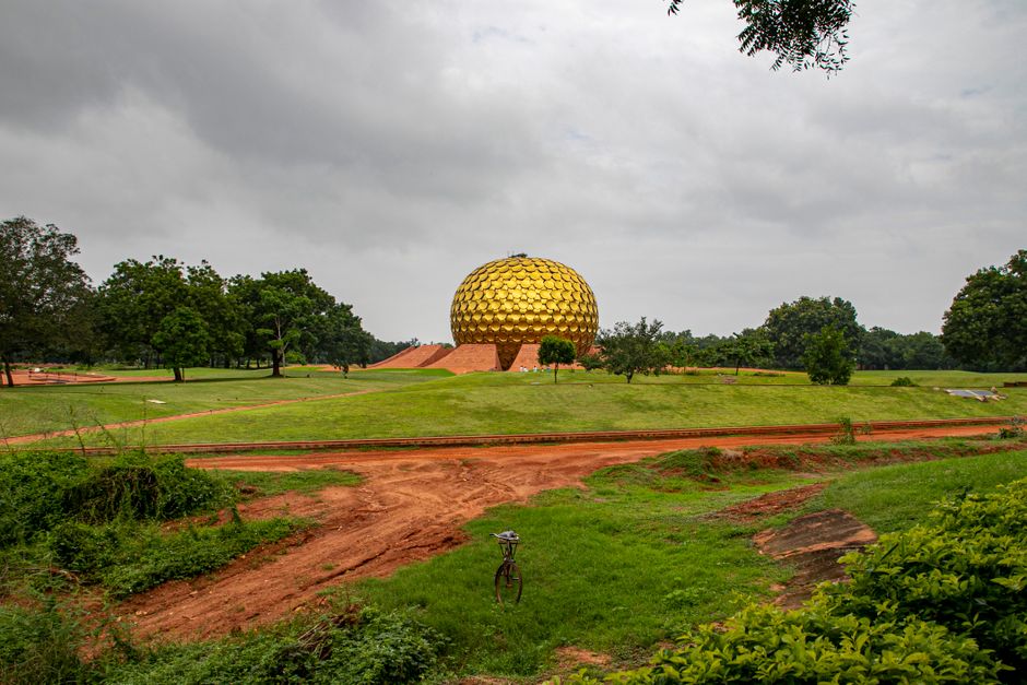 Scenic view of the Matrimandir dome in lush greenery under an overcast sky, Auroville, India.