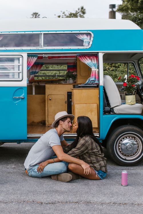 Free A couple sitting affectionately together beside a retro blue van, embracing van life. Stock Photo