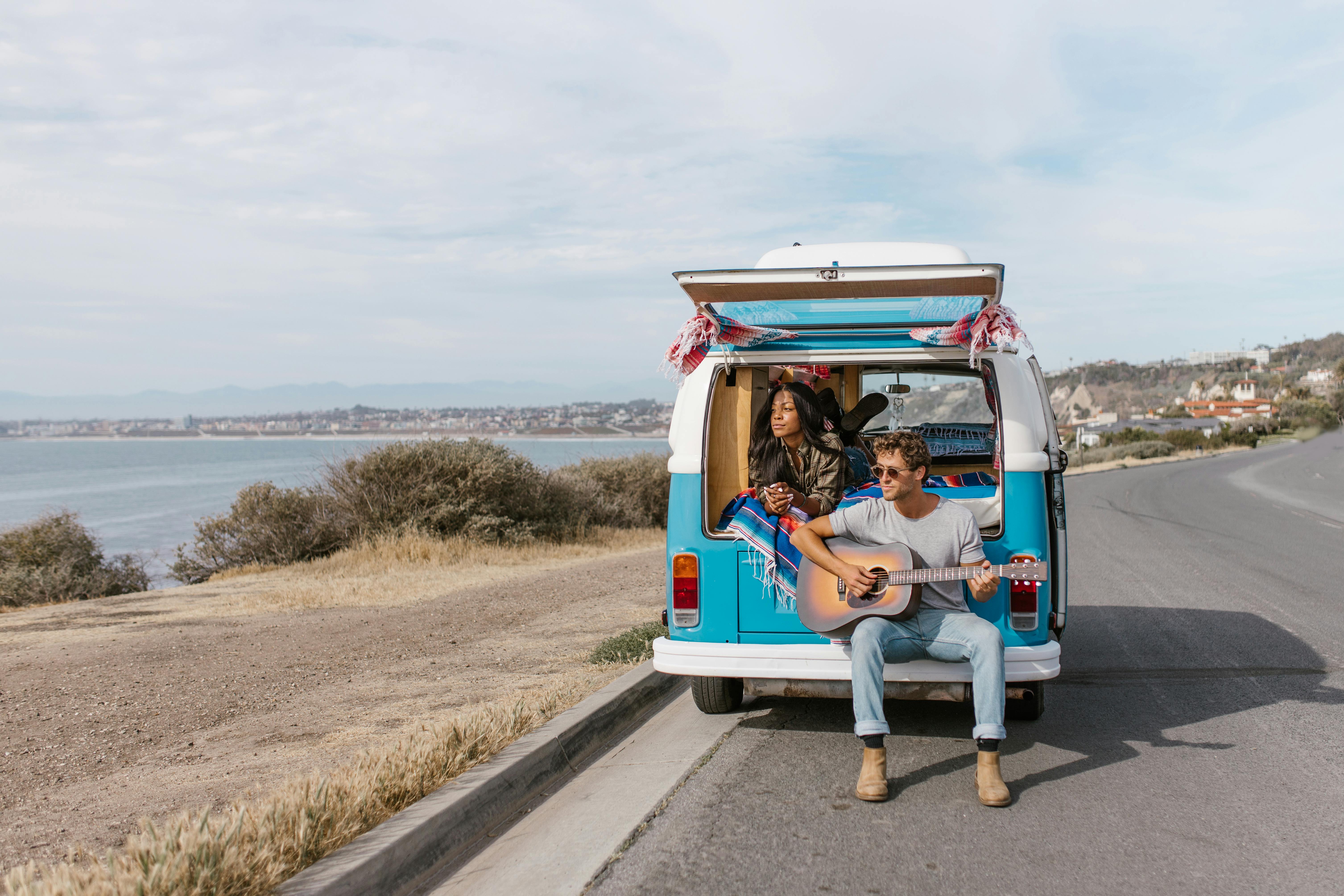 Interracial couple enjoying a coastal road trip in a van. Acoustic guitar sets the relaxed mood.