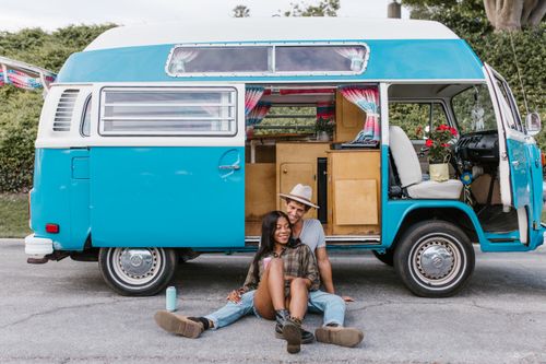 Free Happy couple sitting by a vintage blue van, embracing the joy of van life travel. Stock Photo