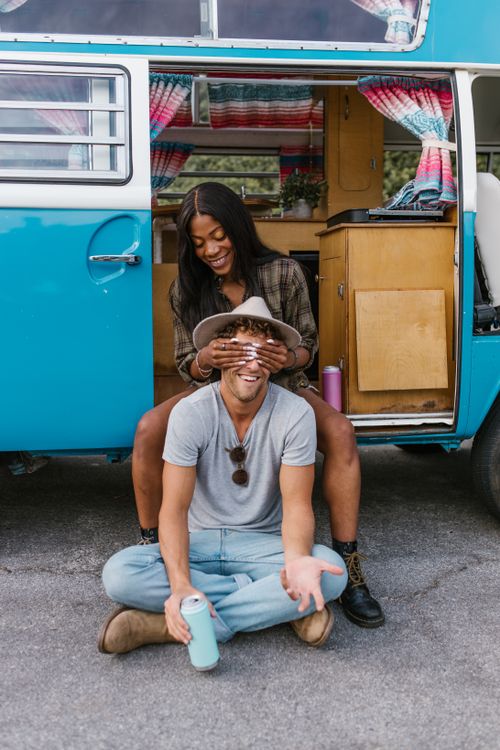 Free Happy couple sitting by campervan enjoying a fun road trip together. Stock Photo