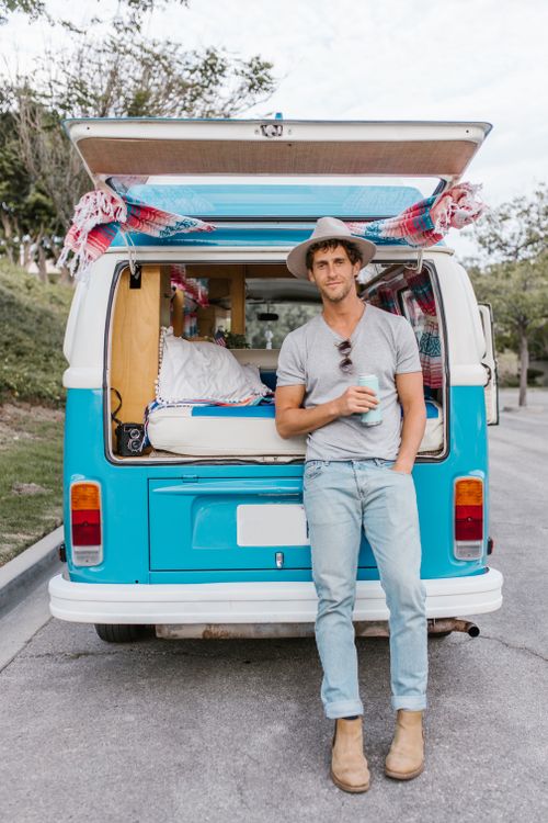 Free Man leaning on blue camper van, enjoying van life outdoors. Stock Photo