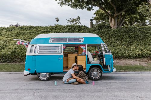 Free Interracial couple sitting by a blue vintage van outdoors, embracing and enjoying van life. Stock Photo