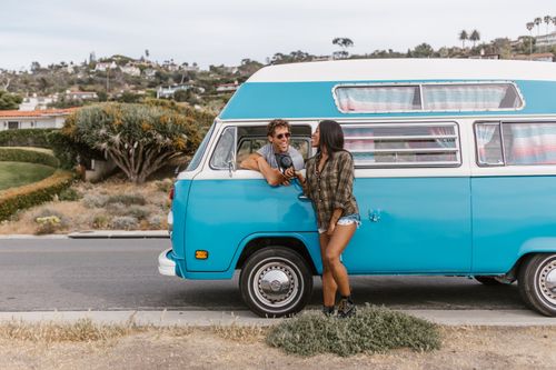 Free Smiling couple relaxes by their iconic blue camper van on a scenic road trip adventure. Stock Photo