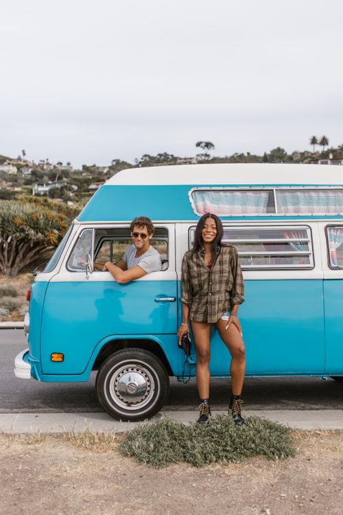 Free Smiling couple enjoying a road trip with a vintage blue campervan, embracing the van life lifestyle. Stock Photo
