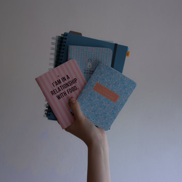 A Person Holding Assorted Notebooks With Slogans On The Covers