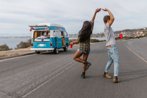 Free A carefree couple dancing by a vintage van on a scenic coastal road. Stock Photo