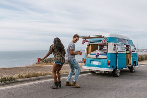 Free Happy couple dancing by their blue campervan on a scenic coastal road trip. Stock Photo