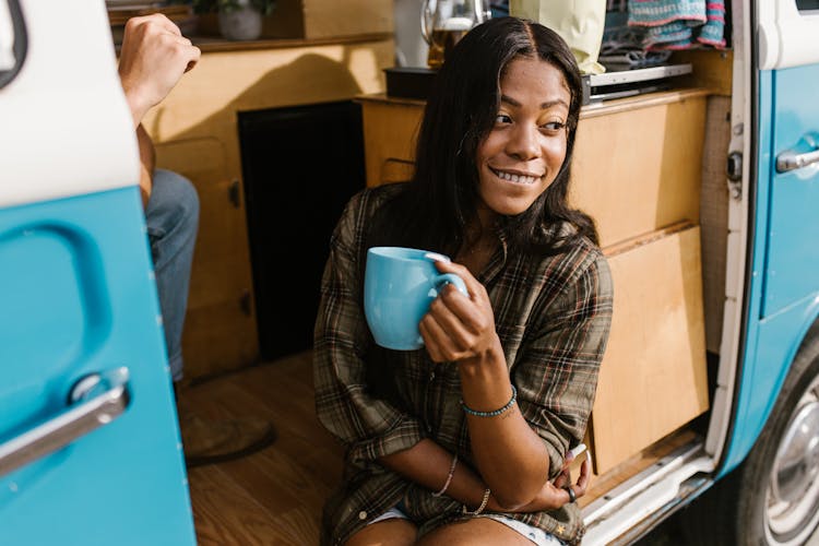 A Woman Holding A Cup Of Coffee While Sitting By The Side Of A Van