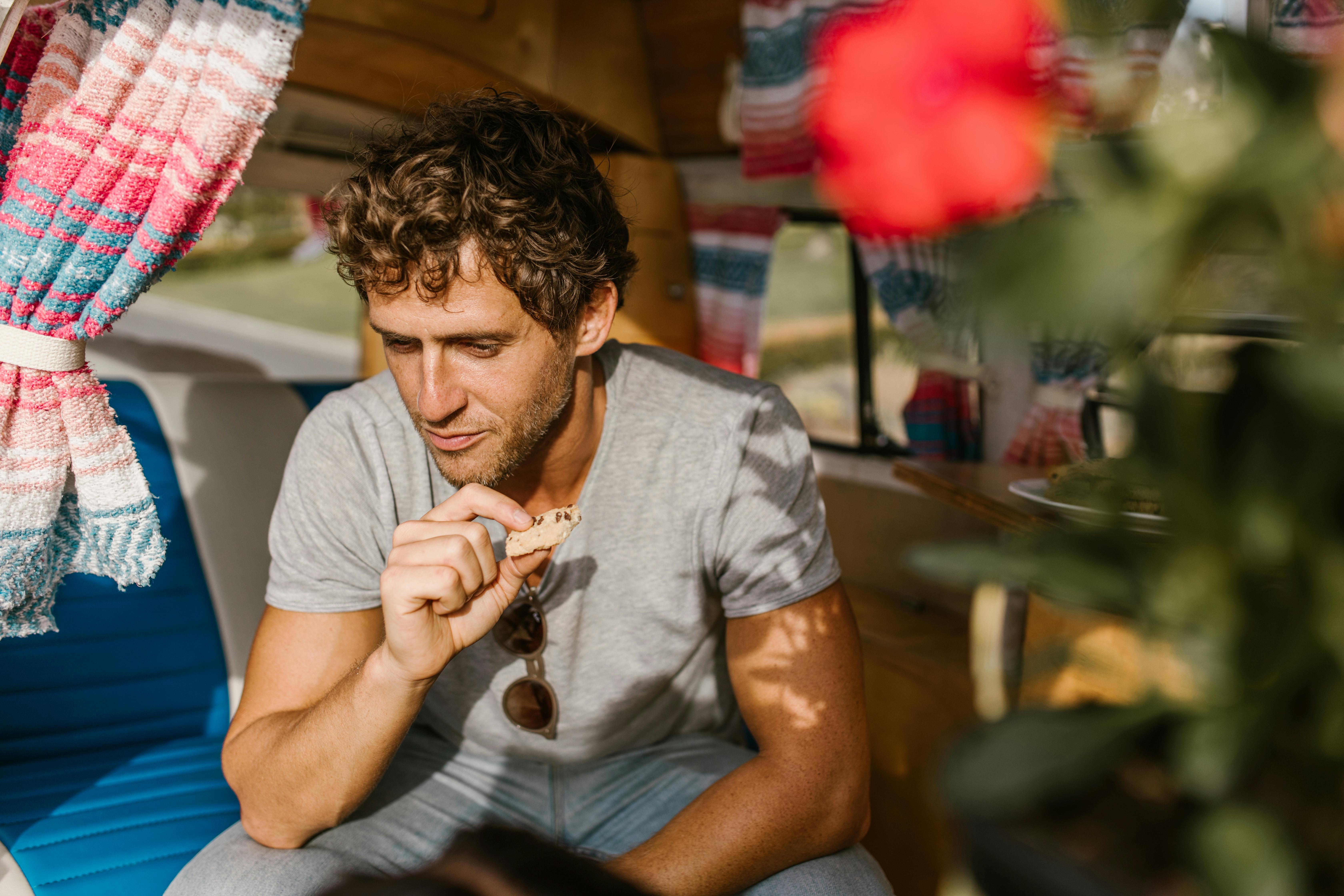 Caucasian man enjoys a snack inside a campervan, surrounded by cozy vibes and sunlight.