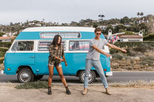 Free Happy interracial couple dancing near a classic blue camper van on a sunny day, showcasing a free-spirited lifestyle. Stock Photo