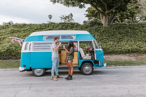 Free A couple enjoys drinks by a classic blue campervan, embracing a carefree travel lifestyle. Stock Photo