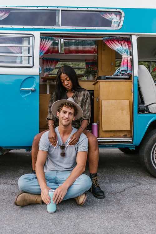 Free An interracial couple enjoying a moment by a vintage camper van, ready for adventure. Stock Photo