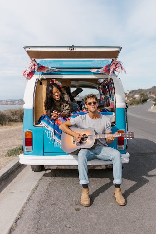 Man Playing a Guitar and Woman Lying in the Back of a Campervan 