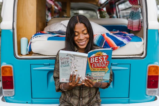 Woman enjoying a book while sitting on a colorful camper van, embracing travel lifestyle.