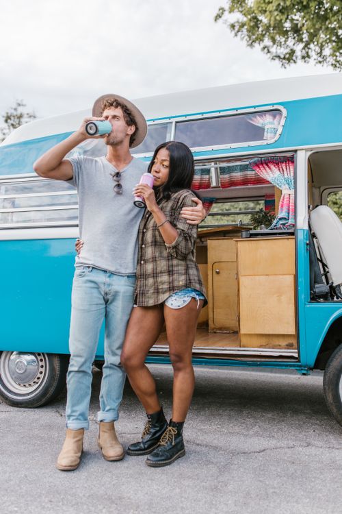 Free Young couple drinking outside a teal vintage van in a relaxed setting. Stock Photo